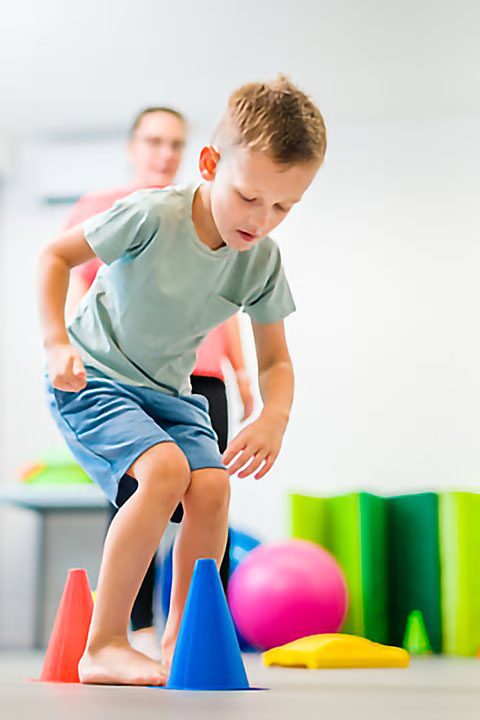 Young boy exercising with female physical therapist during therapy session. Child occupational physical therapy. Bilateral coordination.